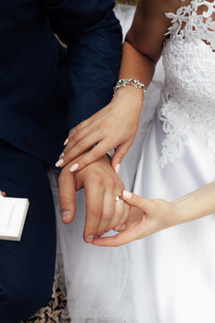 The hands of the bride in a white dress touch the ring on the hand of the groom in a dark blue suit. Image for your creativity, design or illustrations.
