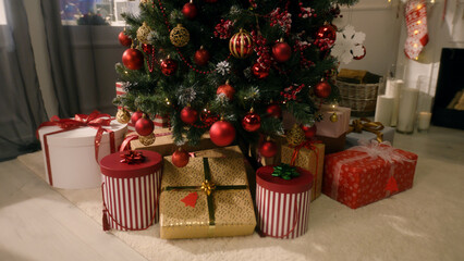 Tree with balls, toys, flashing lights, wrapped gifts and present boxes stands in living room. Christmas and New Year festive interior decoration. Atmosphere in cozy apartment on winter holidays.
