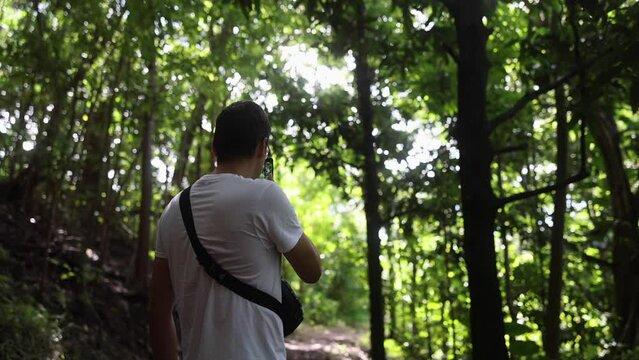 A man using a mobile phone to take pictures of a green forest on a hike 