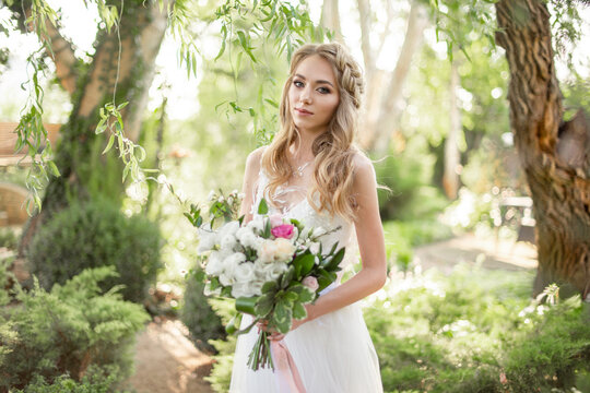 Beautiful woman bride in white wedding dress and bouquet in the garden