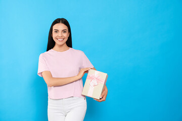 Happy young woman holding gift box on light blue background