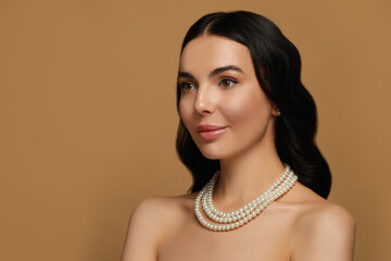 Young woman wearing elegant pearl jewelry on brown background, space for text