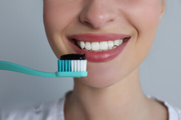 Woman holding toothbrush with charcoal toothpaste on grey background, closeup