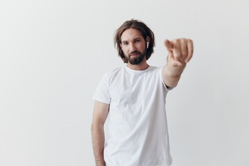 happy man listening to music and smiling in a white t-shirt on a white background and pointing a...