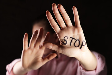 Woman with word Stop written on hand against dark background, closeup. Domestic violence concept