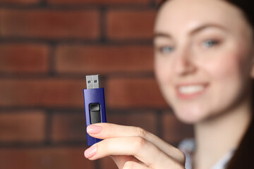 Woman holding usb flash drive near brick wall, focus on hand