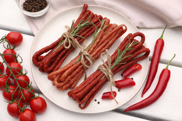 Bundles of delicious kabanosy with rosemary, peppercorn, chilli and tomatoes on white wooden table, above view