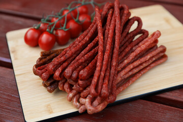 Tasty dry cured sausages (kabanosy) and tomatoes on wooden table, closeup