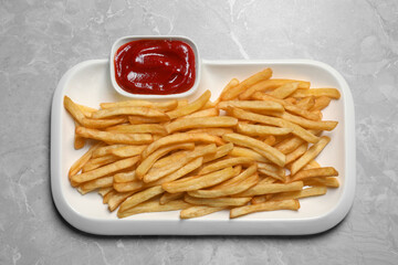 Plate of tasty french fries served with ketchup on light grey marble table, top view