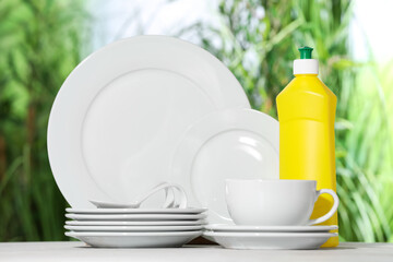 Set of clean dishware and detergent on white table against blurred background