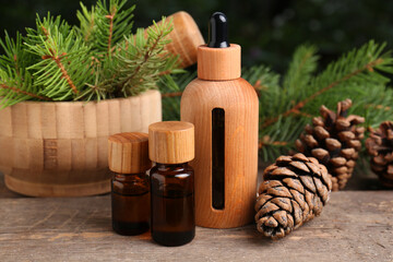Fototapeta na wymiar Bottles of pine essential oil, conifer tree branches and cones on wooden table