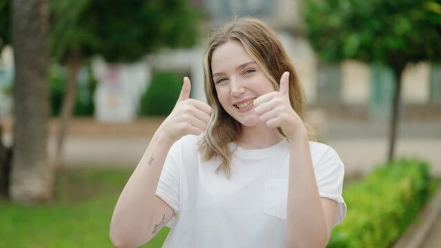 Young caucasian woman smiling confident doing ok sign with thumbs up at park