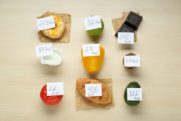 Food products with calorific value tags on wooden table, flat lay. Weight loss concept