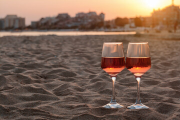 Glasses of tasty rose wine on sandy beach, space for text