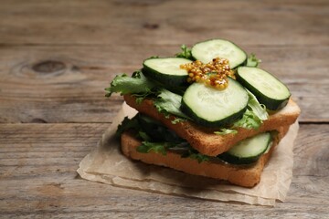 Tasty cucumber sandwiches with arugula and mustard on wooden table