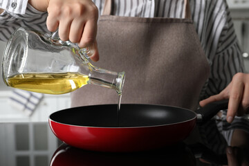 Woman pouring cooking oil from jug into frying pan on stove, closeup