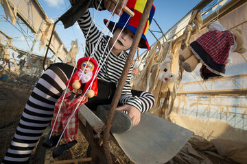 Young clown with scary smile  plays and has fun in an abandoned greenhouse with a puppet and plush toys