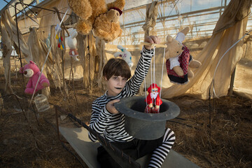 Young clown with scary smile  plays and has fun in an abandoned greenhouse with a puppet and plush toys