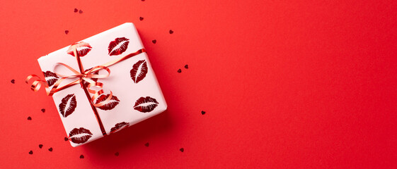Saint Valentine's Day concept. Top view photo of large present box in wrapping paper with kiss lips pattern and confetti on isolated red background with copyspace