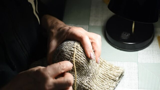 The video shows how a woman darns a woolen sock with a large needle and woolen thread.