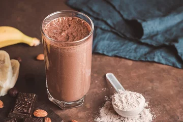 Poster Chocolate milkshake smoothie with banana, protein powder and nuts on dark background © O.Farion