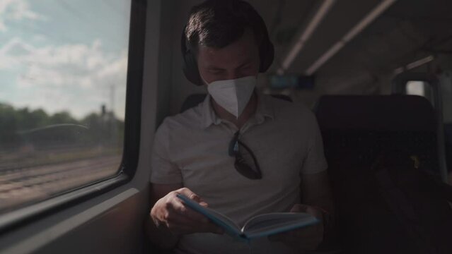 Passenger traveling on Deutsche train in summer with wireless headphones and reading book. Student reads study workbook with wireless earphones while commuting on train. Daily commute to university. 