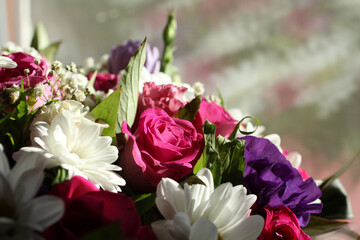 A bouquet of pink roses, lilac flowers of Alstroemeria and white small chrysanthemums, standing near the window and lit by the sun's rays