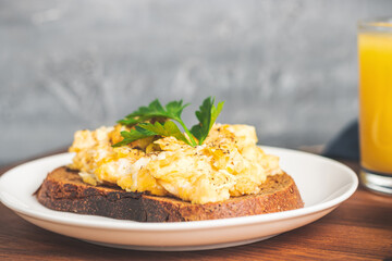 Scrambled eggs with parsley on bread at white plate, homemade healthy breakfast on wooden board