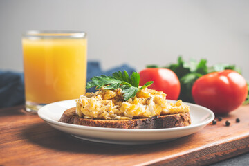 Scrambled eggs with parsley on bread at white plate, homemade healthy breakfast on wooden board