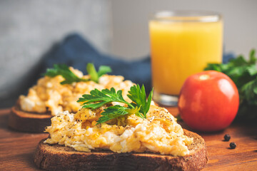 Scrambled eggs with parsley on bread, homemade healthy breakfast on dark wooden board
