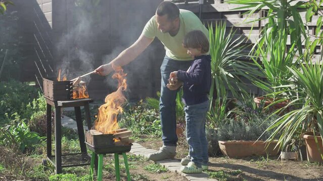 Man and son put wood pieces on barbecue grill fire