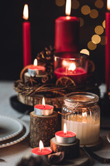 Rustic table decor for Christmas or New Year family dinner. Centrepiece with red candle, dry orange, cone, cinnamon, anise. Zero waste eco-friendly home. Cozy atmosphere, dark background. Close up