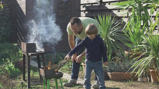 Man teaches son to prepare grill fire for the backyard barbecue