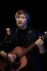 Obraz premium Male musician with guitar in hands playing and posing on black background in blue scenic light