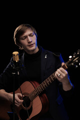 Male musician with guitar in hands playing and posing on black background in blue scenic light