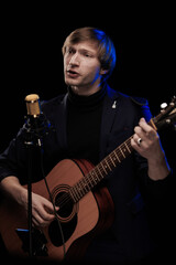 Obraz premium Male musician with guitar in hands playing and posing on black background in blue scenic light