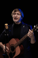 Obraz premium Male musician with guitar in hands playing and posing on black background in blue scenic light