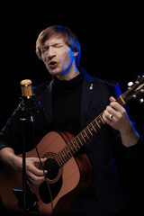 Male musician with guitar in hands playing and posing on black background in blue scenic light