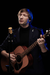 Obraz premium Male musician with guitar in hands playing and posing on black background in blue scenic light