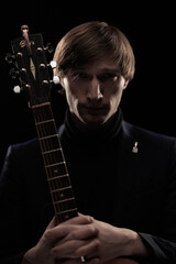 Male musician with guitar in hands playing and posing on black background in blue scenic light