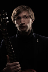 Male musician with guitar in hands playing and posing on black background in blue scenic light