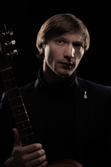 Male musician with guitar in hands playing and posing on black background in blue scenic light