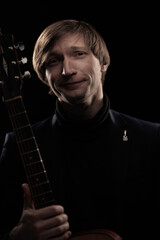 Male musician with guitar in hands playing and posing on black background in blue scenic light