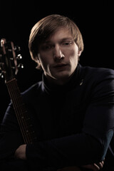 Male musician with guitar in hands playing and posing on black background in blue scenic light