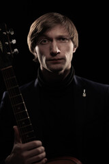 Obraz premium Male musician with guitar in hands playing and posing on black background in blue scenic light