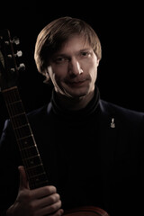 Male musician with guitar in hands playing and posing on black background in blue scenic light