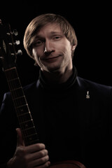 Male musician with guitar in hands playing and posing on black background in blue scenic light