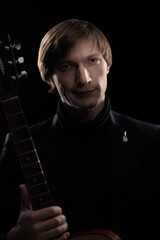 Male musician with guitar in hands playing and posing on black background in blue scenic light