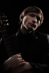 Male musician with guitar in hands playing and posing on black background in blue scenic light