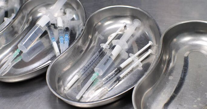 On the table are trays with syringes filled with medicines for injection. The doctor puts another syringe with medicine into the tray with a gloved hand. Injection preparation concept.